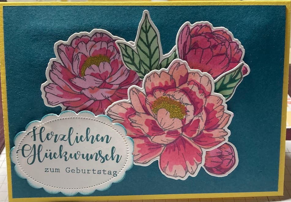 Eine Karte mit blauem Hintegrrund und drei großen, roten Blüten aus Papier. Die Aufschrift lautet " Herzlichen Gkückwunsch zum Geburtstag"