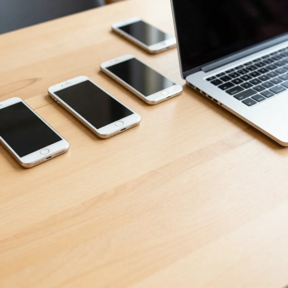 Auf einem Tisch steht ein Laptop. Um ihn herum liegen 4 Handys.